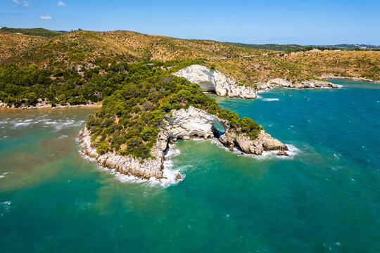 A vibrant aerial view of Torre di San Felice perching on the dramatic cliffs of Gargano in Puglia, Italy. The ancient watchtower stands above turquoise Adriatic waters, surrounded by green hills