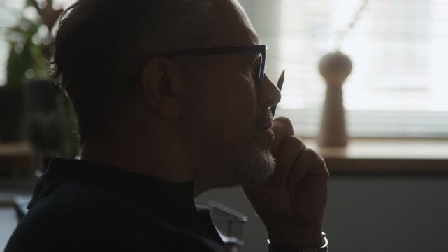 Middle aged Caucasian man wearing eyeglasses holding pencil near face, thinking deeply listening to client in therapy session. Clip for mental health counseling and professional psychology campaigns