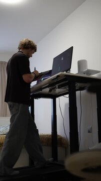 Vertical screen student takes notes while walking on a treadmill and learning video editing at a computer combining study with an active routine at home