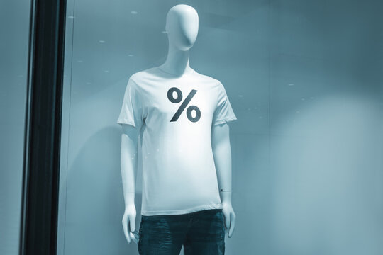 Mannequin standing in a retail store window, wearing a white t shirt with a percent sign, symbolizing sales and discounts