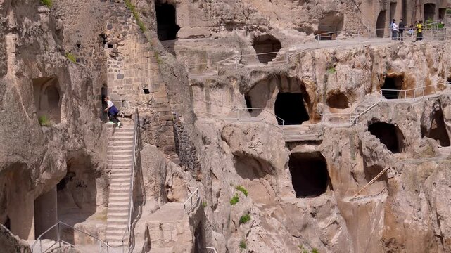 Curious tourists wandering through the ancient vardzia cave city, a historic monastery complex carved into the erusheti mountain, exploring its many rooms, tunnels, and stairways in georgia