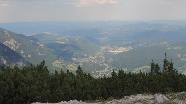 The camera shows a wide view of green hills and a valley under a bright sky.