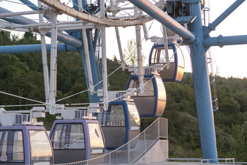 Enclosed gondola cabins line a cable system beside blue steel towers, with numbered cars ascending above railings and wooded hills beyond © Anat art
