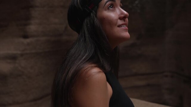 Close-up portrait of a smiling young woman wearing a headlamp as she looks up in wonder at the rock walls of a dark cave.