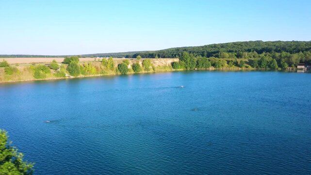 The lake is located in an abandoned quarry with blue water. Scenic aerial view of an abandoned quarry with clear blue water transformed into a public beach and recreational park with swimmers.