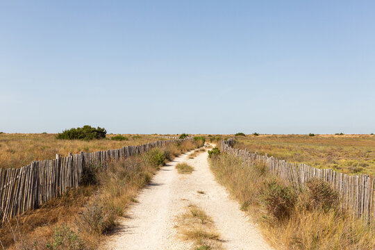 Chemin de sable bord&eacute; de cl&ocirc;tures en bois et de garrigue sous un ciel bleu