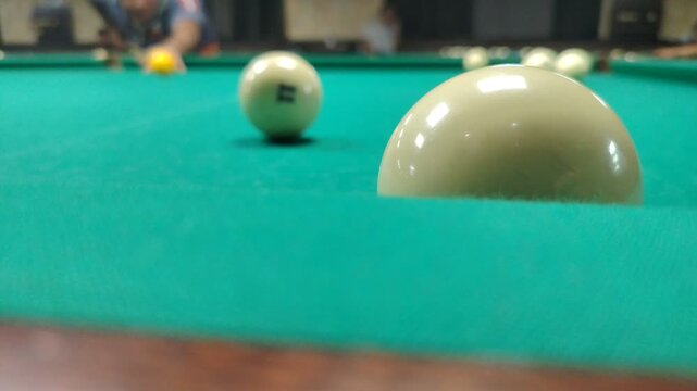 Player hitting billiard balls on a green table during a game. Close-up of billiard balls rolling on a green table during a game indoors