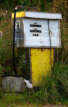Abandoned rusty vintage fuel pump overgrown by vegetation