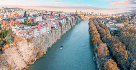 Tbilisi cityscape with a panoramic view of the Old Town, buildings on cliffs, the Kura river, and golden autumn trees © EdNurg