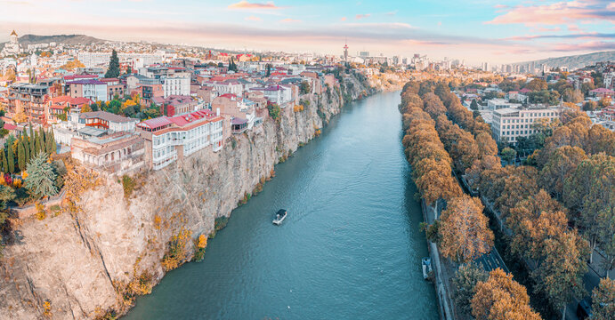 Tbilisi cityscape with a panoramic view of the Old Town, buildings on cliffs, the Kura river, and golden autumn trees