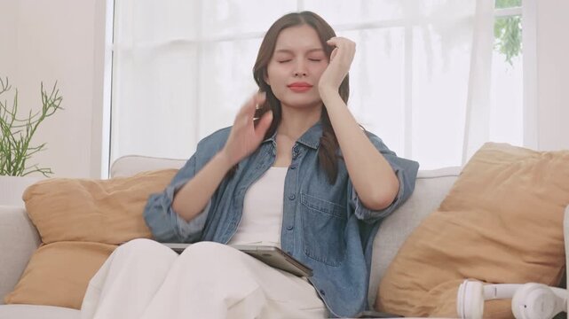 Tired young Asian woman closing her laptop, rubbing her eyes, and stretching after working from home.