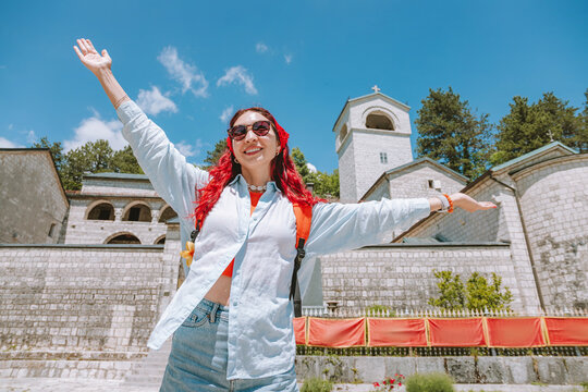 Female tourist with backpack exploring Cetinje Monastery in Montenegro, arms spread wide embracing travel and freedom