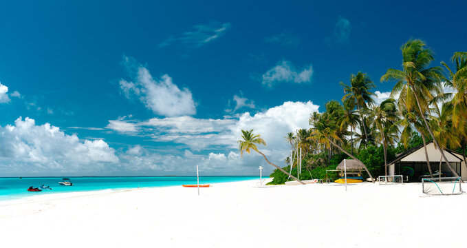Tropical luxury beach resort with white sand, beach umbrellas, sun loungers, palm trees and turquoise ocean water