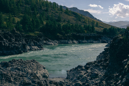 Mountain river canyon with dark rocky shores and forested hills