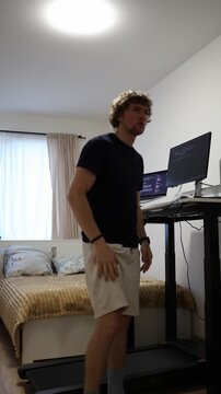 Vertical screen exhausted remote worker steps off his walking treadmill and takes a break after working too long at the computer feeling drained by a demanding workday at home