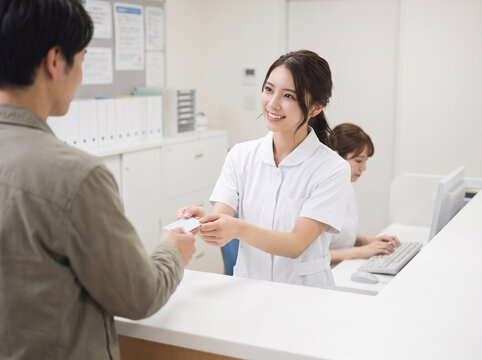 受付で診察券を差し出す男性に対応する笑顔の看護師