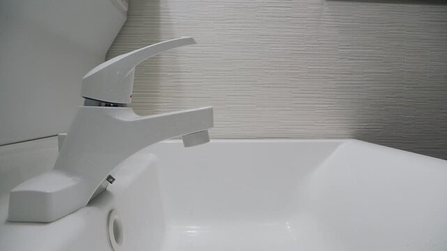 Hand closes a dripping faucet firmly to stop wasting water