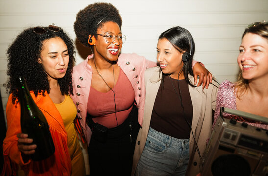 Group of multiracial girls dancing, drinking champagne and listening music outdoor - Party, new year's eve and street nightlife concept - Main focus on center right girl face - UGC flash content