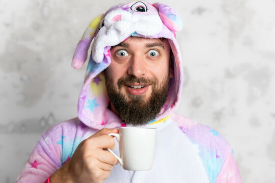 Cheerful man in a colorful unicorn onesie smiling and holding a white mug, with a world map background. Fun, playful concept for lifestyle or creative projects.