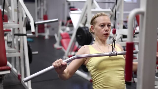 In this close-up video, watch a middle-aged woman engage in pulldown training on a lat machine, showcasing her commitment to fitness and the importance of strength training in the gym.