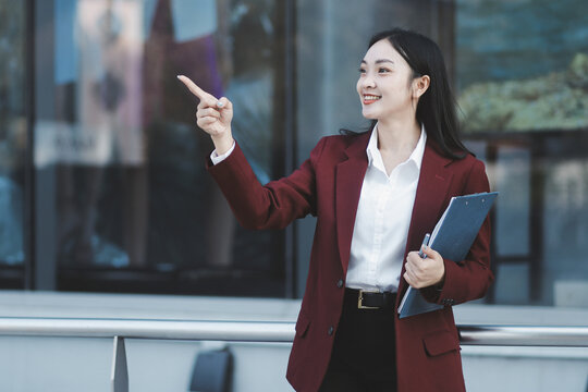 Young professional woman talking on phone and holding coffee outside modern office building
