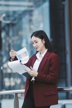Young professional woman talking on phone and holding coffee outside modern office building