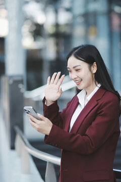 Young professional woman talking on phone and holding coffee outside modern office building