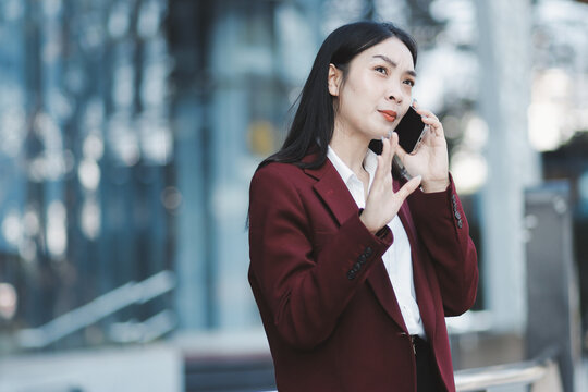 Young professional woman talking on phone and holding coffee outside modern office building
