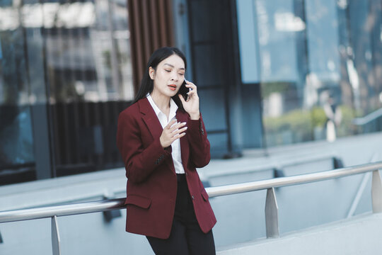 Young professional woman talking on phone and holding coffee outside modern office building