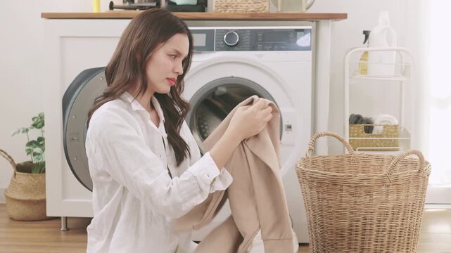 Frustrated young Asian woman sitting on the floor feeling stressed and overwhelmed by a pile of laundry.	