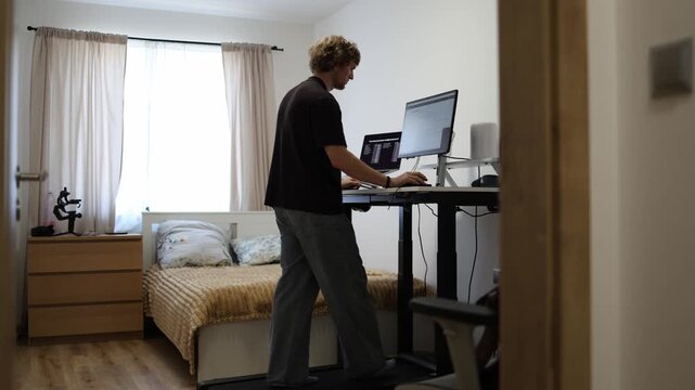 Young man continues working after his regular job while walking on a treadmill and completing computer tasks at home combining extra work hours with daily physical activity