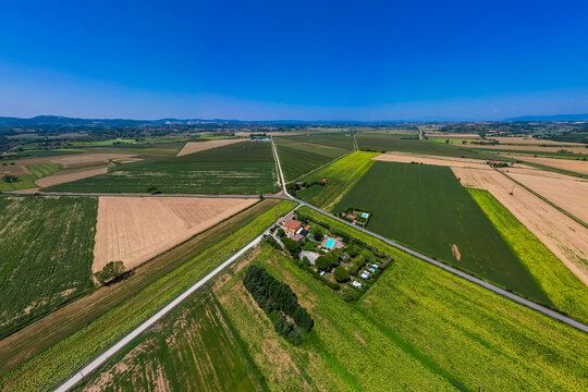 An aerial drone view reveals a charming Tuscan agriturismo nestled among vibrant sunflower fields and vast farmland. The property features a swimming pool and an organized camperstop for motorhomes in