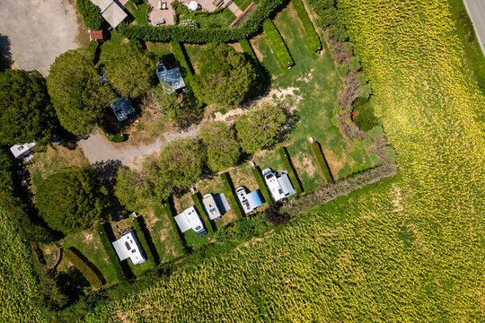 An aerial drone view reveals a charming Tuscan agriturismo nestled among vibrant sunflower fields and vast farmland. The property features a swimming pool and an organized camperstop for motorhomes in
