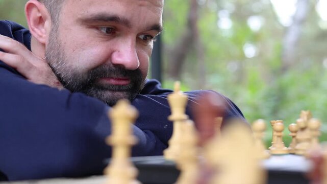 Dolly shot of a man is looking at the chessboard. His eyes are scanning the board - he is analyzing the position of the pieces on the chess field and thinking through his next move. Slow motion 4k foo