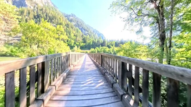 Insta360 moving low above a wooden bridge trail through the forest, then rising to reveal the Enns River, lush green landscape and surrounding hills near Admont.