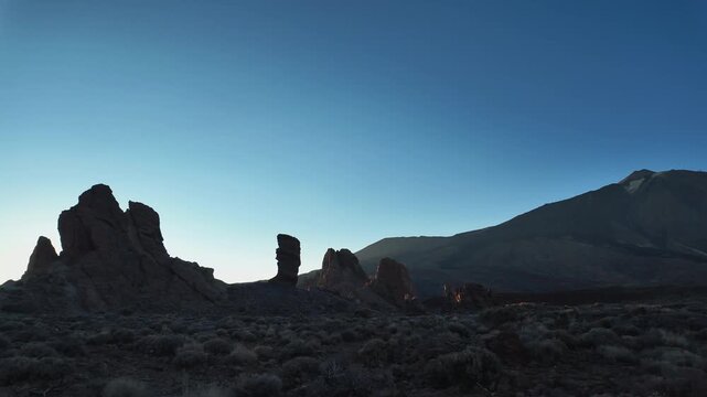Silhouettes of the volcanic rock formations of Roques de Garcia against a deep blue dawn sky in Teide National Park, Tenerife, Canary Islands.