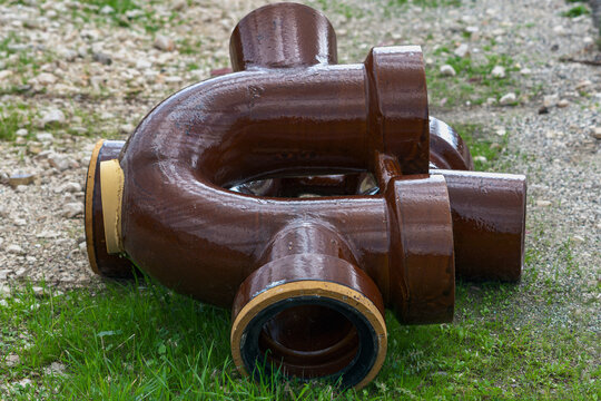 Glazed ceramic stoneware sewer siphon fittings with natural glaze texture on grass and gravel, low angle view, new vitrified clay drainage pipes in a storage yard, shallow depth of field.