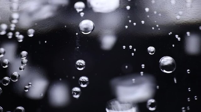 Numerous sparkling water bubbles form bright, reflective spheres across a glossy black surface, creating a dramatic abstract pattern.