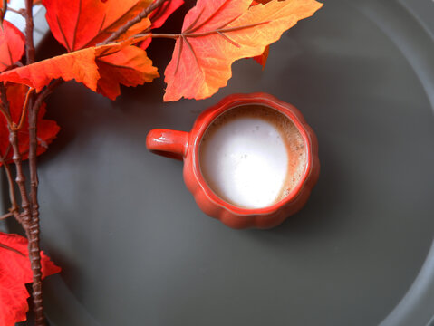 A warm cup of coffee served in an orange cup, surrounded by cozy autumn decorations. The image represents autumn, warmth, comfort, seasonal decor, relaxation, and a cozy atmosphere.