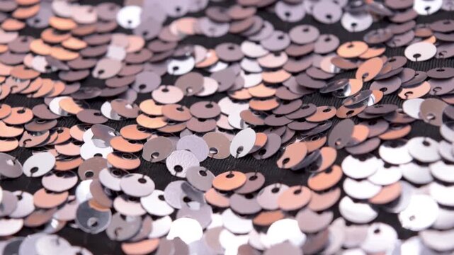 Close-up rotating shot of shimmering silver and orange sequins on black fabric background, highlighting texture and light reflection