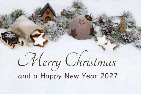 Christmas card with the text "Merry Christmas and a Happy New Year 2027," decorated with cinnamon star cookies, a Christmas bauble, and a wooden sled in the snow.