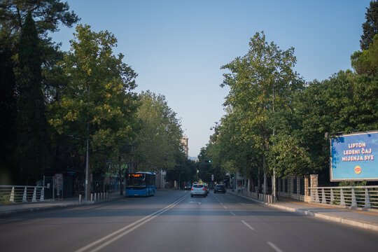 Cars and a public bus drive down a wide, tree-lined avenue under a clear blue sky in Podgorica, Montenegro on August 12, 2026