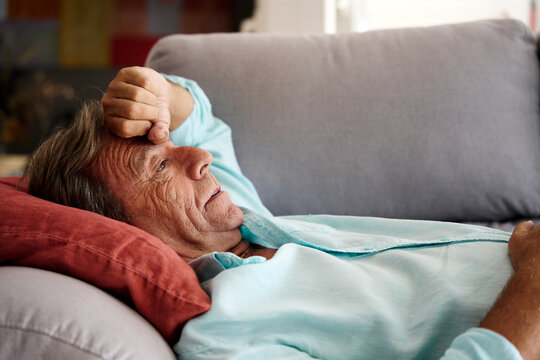 Senior man rests on sofa with a headache