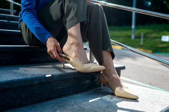 Woman sits on stairs removing her high heel shoe due to fatigue