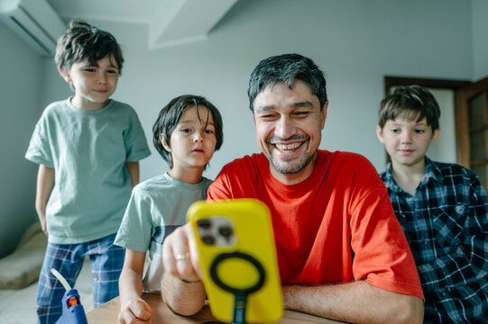 A father and his sons watch videos on a smartphone at home