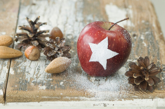 Christmas apple with snow star, pine cones, almonds and hazelnuts on table