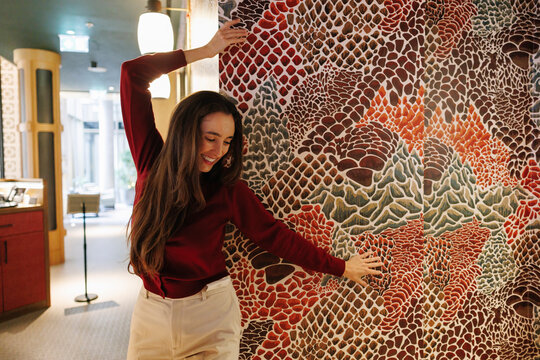 Young woman in red sweater dances happily against patterned hotel wall