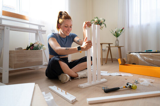 Smiling woman assembles wooden furniture on the floor at home