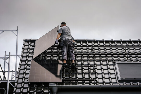 Roofer installs a solar panel on a tiled roof during modernization