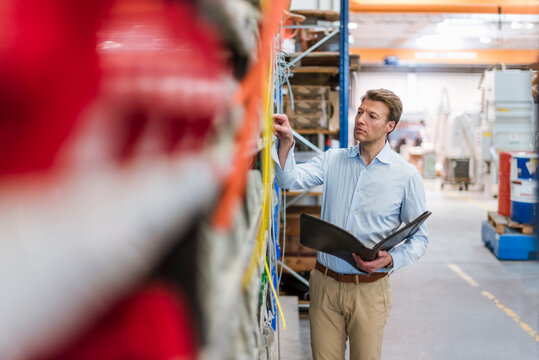 Man in factory storeroom holding folder checking shelf